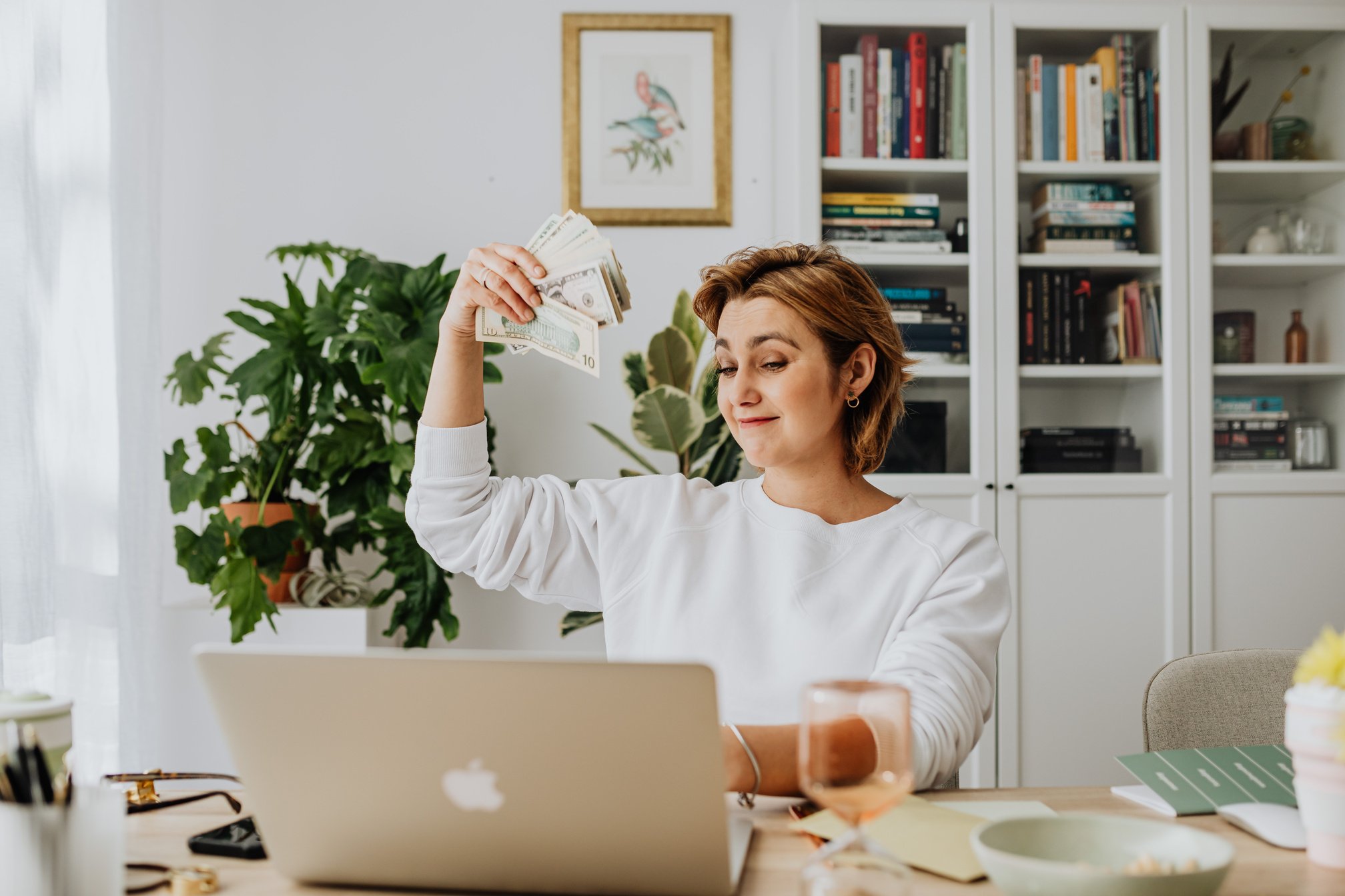 Woman Sitting in an Office in front of a Laptop and Waving CashÂ